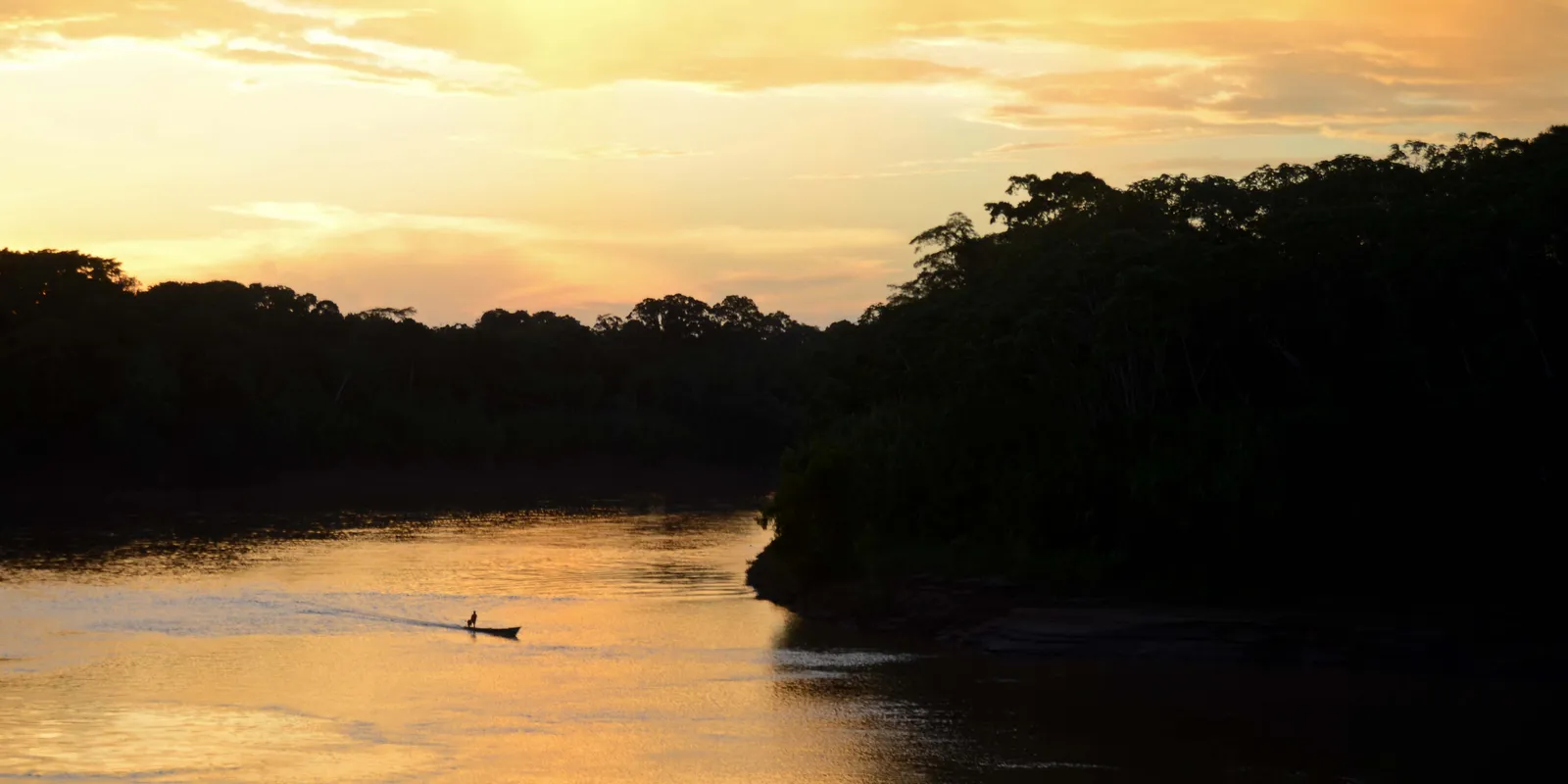Canoa en el río Tambopata al atardecer, entre orillas cubiertas de bosque amazónico